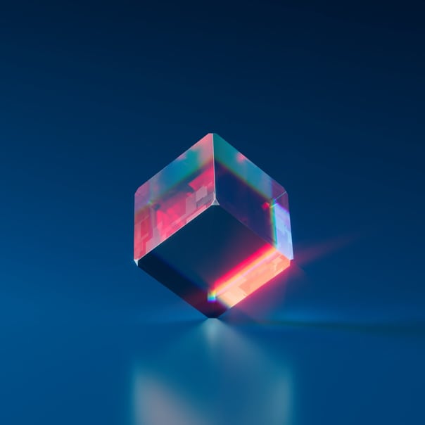 A glass cube on a flat surface with a rainbow reflection and a bright red light inside, creating a stunning spectrum of colors